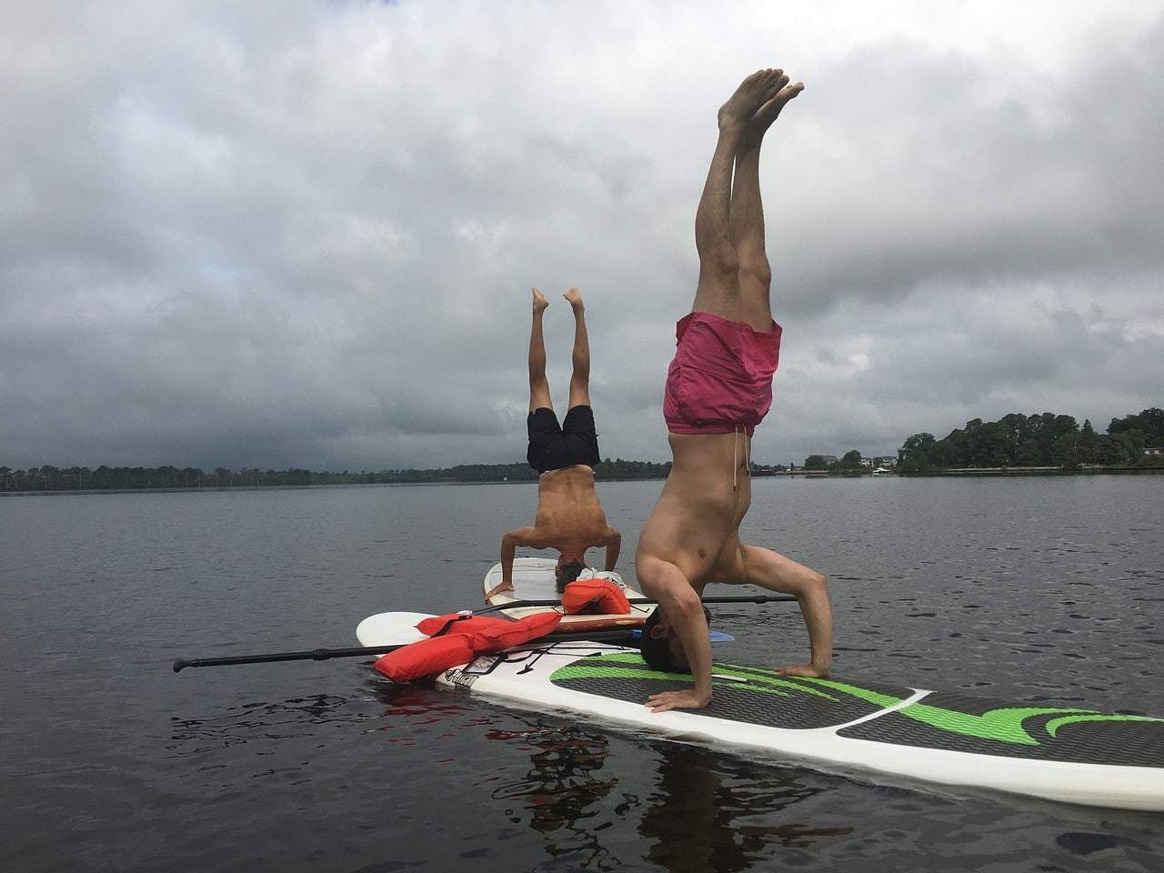 two paddlers doing yoga head stands on a paddle board