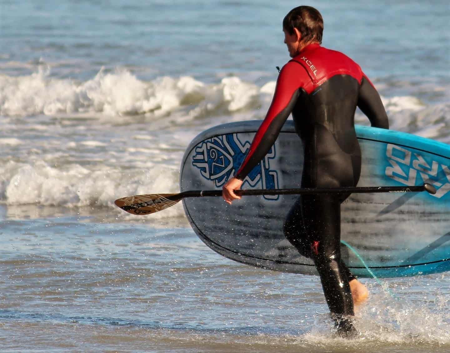 paddle boarder in a wetsuit carrying a paddle board